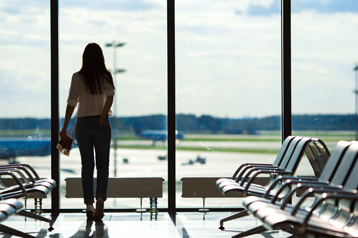 Junge Frau in einem Flughafen-Lounge in der Nähe des Fensters, wartend auf ihren verspäteten Flug.